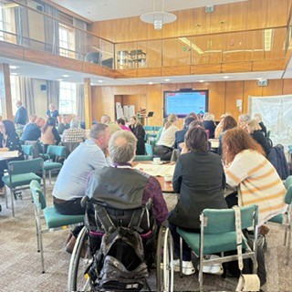 image of people sat on chairs around a table and a presentation on a projector at the front of the room